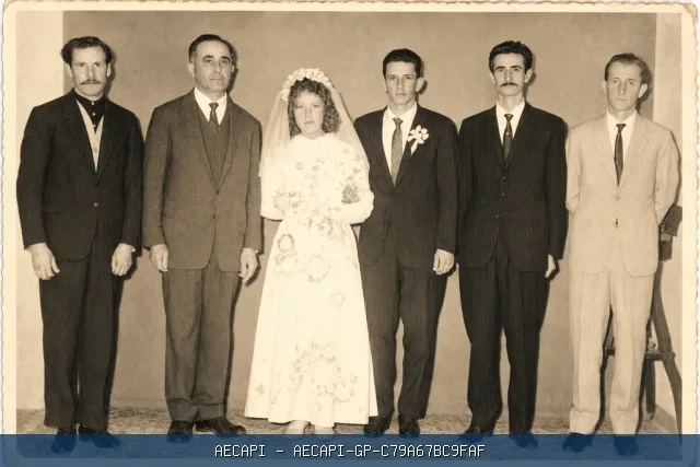 Casal em trajes de casamento posando com quatro homens em uma fotografia histórica.